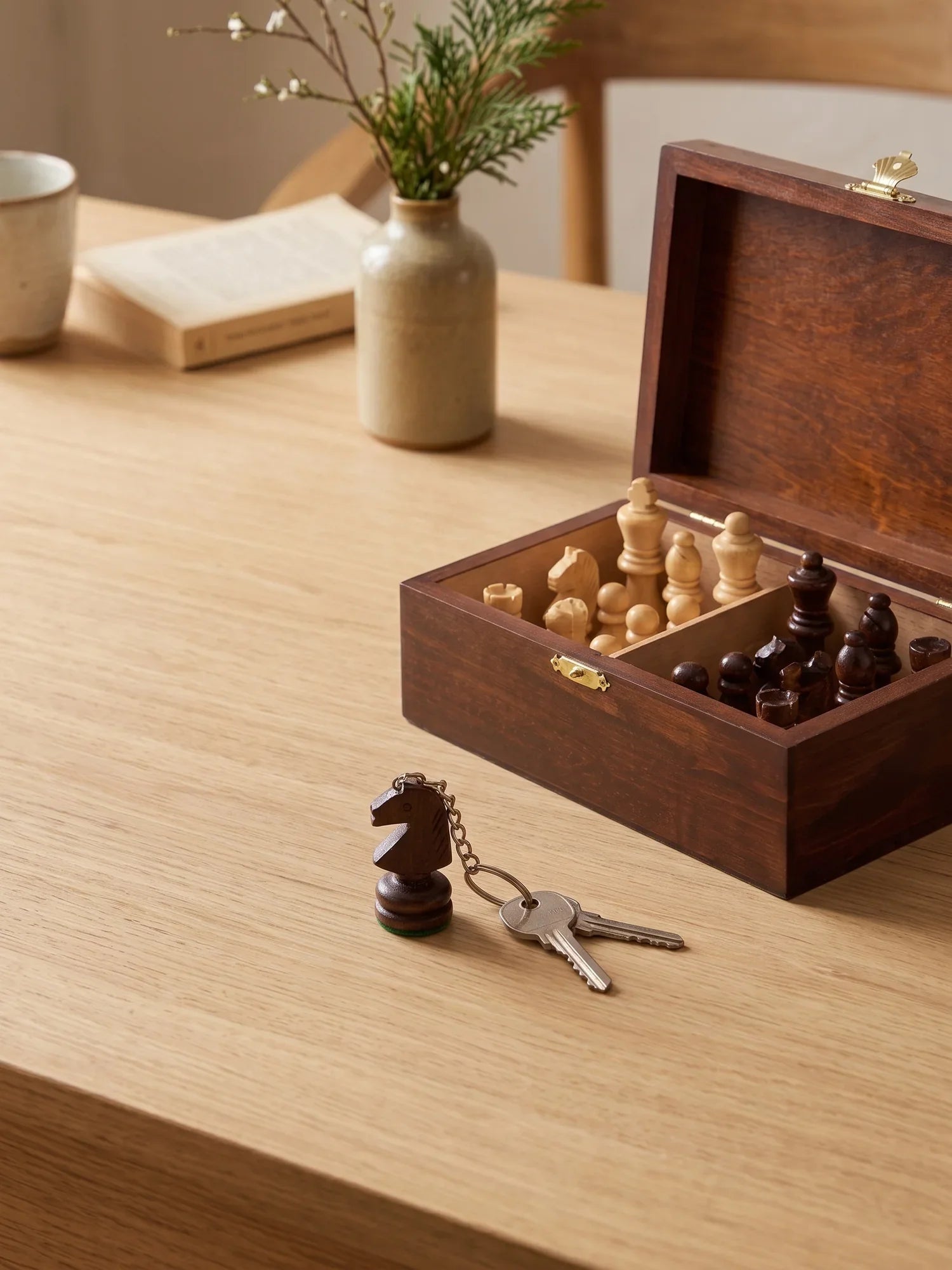 Boîte de rangement en bois ouverte avec des pièces d’échecs, et un porte-clés cavalier posé à côté de clés