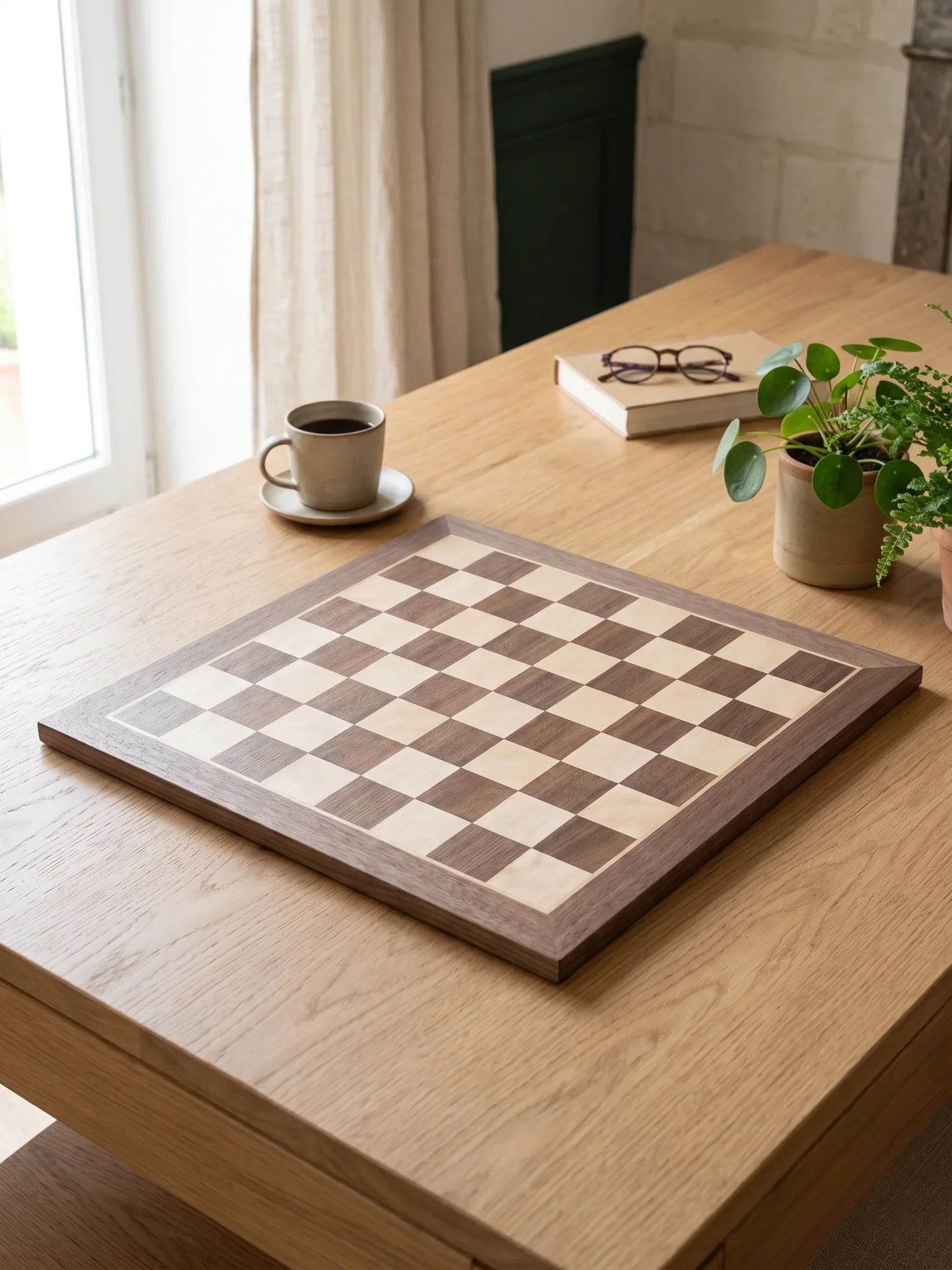 Plateau d’échecs en bois sans pièces, posé sur une table en chêne près d’une fenêtre
